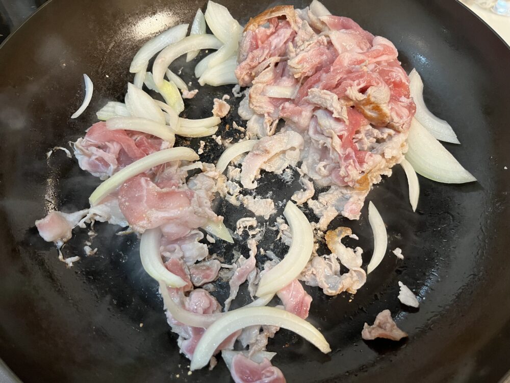 鉄フライパンで肉と玉ねぎを焼いている。一部フライパンにくっついている。